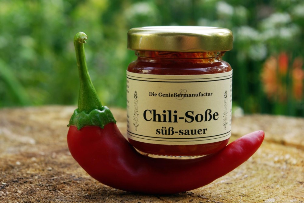 Süß-sauer-Dip. Ein Glas Chilisoße süß-sauer steht auf einer roten Chili.