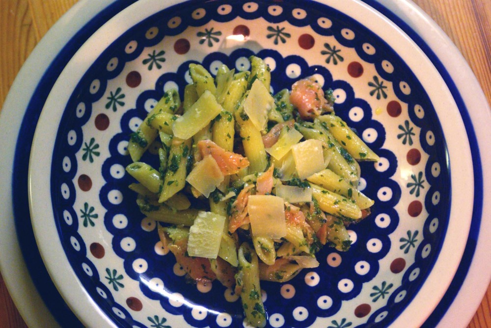 Zitronenpasta mit Lachs. Auf einem Teller mit Bunzlauer-Motiv sind breite Nudeln mit der Zitronen-Petersilienmischung angerichtet. Obenauf zieren breite Parmesanspäne und der zerzupfte Räucherlachs die Pasta.