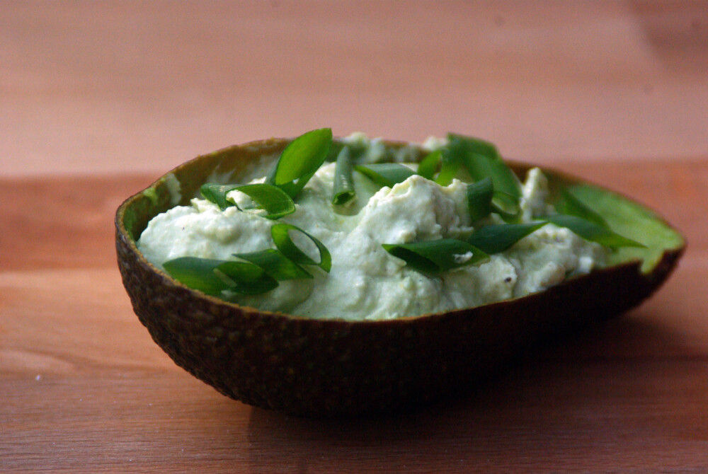 Avocado-Creme in vier Variationen - In einer ausgekratzten dunkelbraunen Schale einer Avocado wurde die Avocado-Creme gefüllt, garniert mit Ringen der grünen Zwiebelschlutte