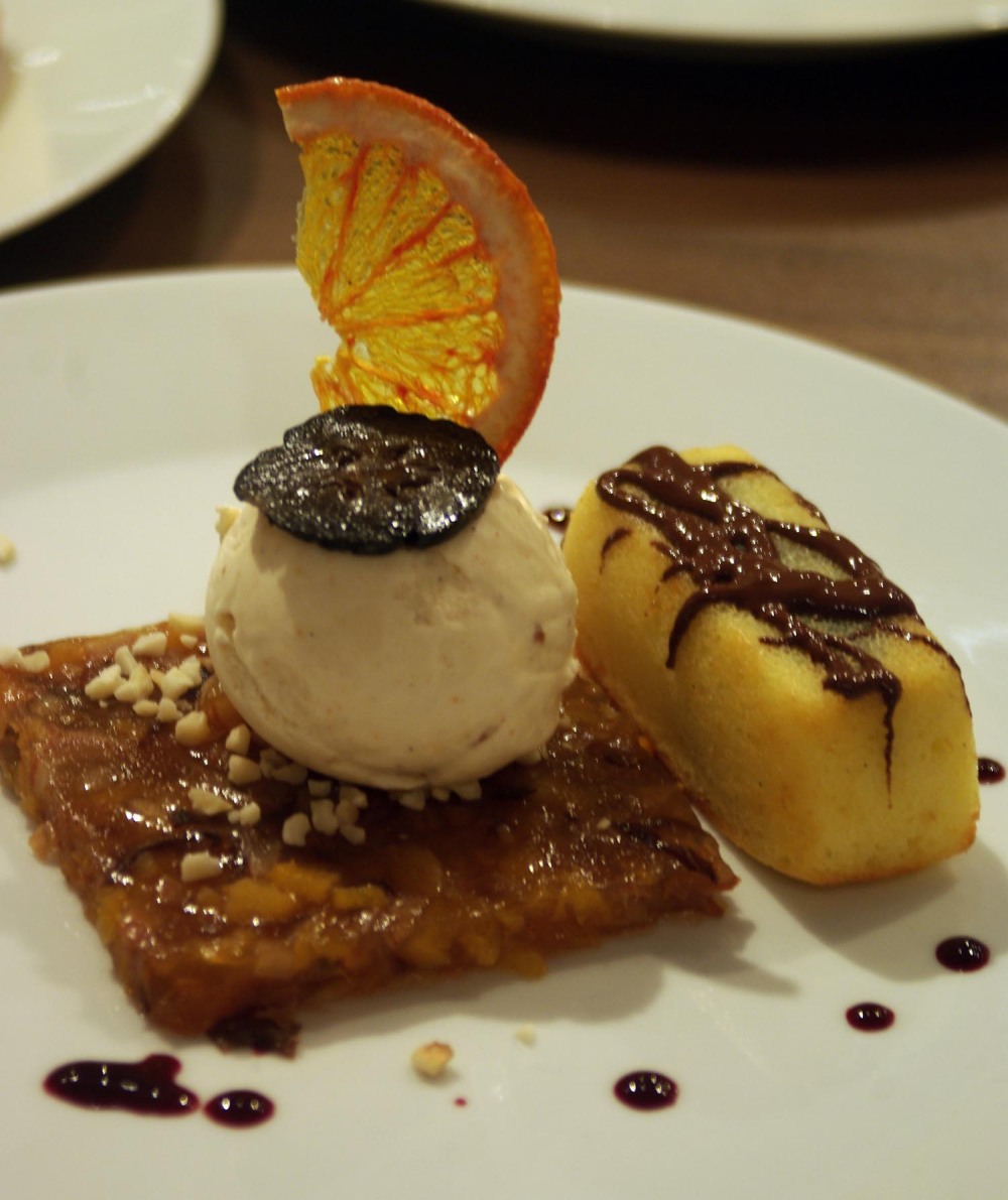 Eis des Maharadscha. Eine Kugel Eis auf Quadrat gelierten Obstsalats, garniert mit halber kandierter Orangenscheibe, daneben ein Stück Orangenkuchen.