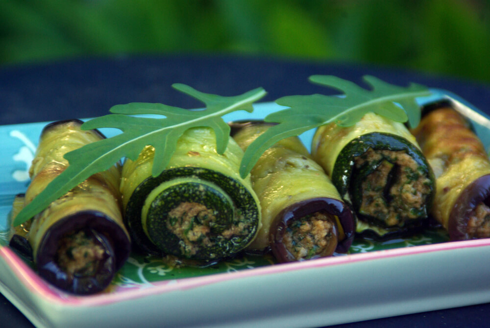 Auberginen und Zucchini in Scheiben geschnitten und gegart. Mit einer Walnuss-Knoblauch-Paste gefüllt und zu Röllchen gedreht, auf einem rechteckigen Tellerchen angerichtet und mit Rucola garniert.