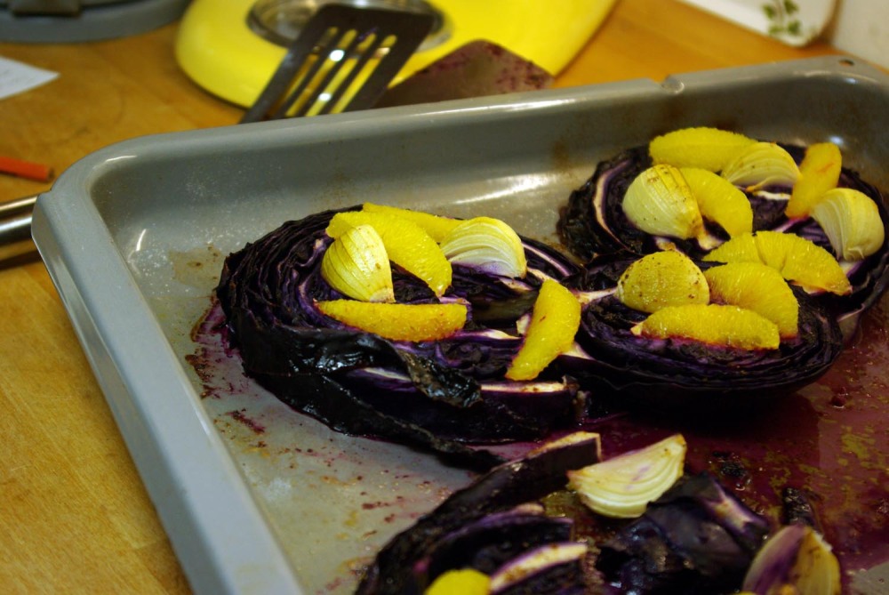 Blaukraut oder Rotkohl in Scheibengeschnitten liegen auf dem Backblech. Das Blaukraut ist gegart und obenauf mit Zwiebelvierteln garniert.