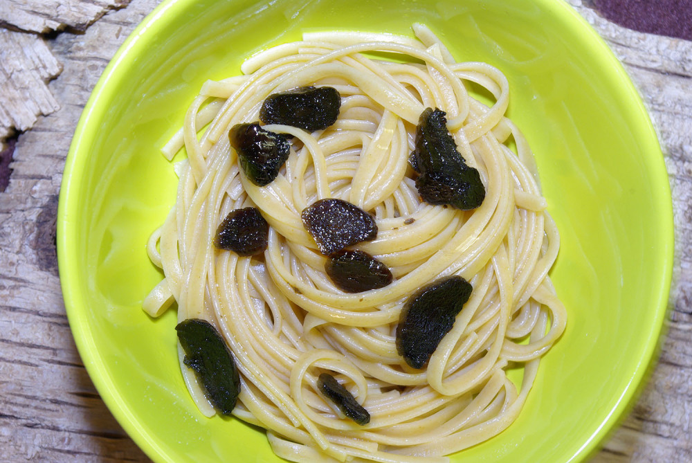 Pasta Aglio e Olio und Schwarzer Knoblauch. Lindgrüner Teller, darauf Spaghetti, garniert mit Scheiben vom Schwarzen Knoblauch.