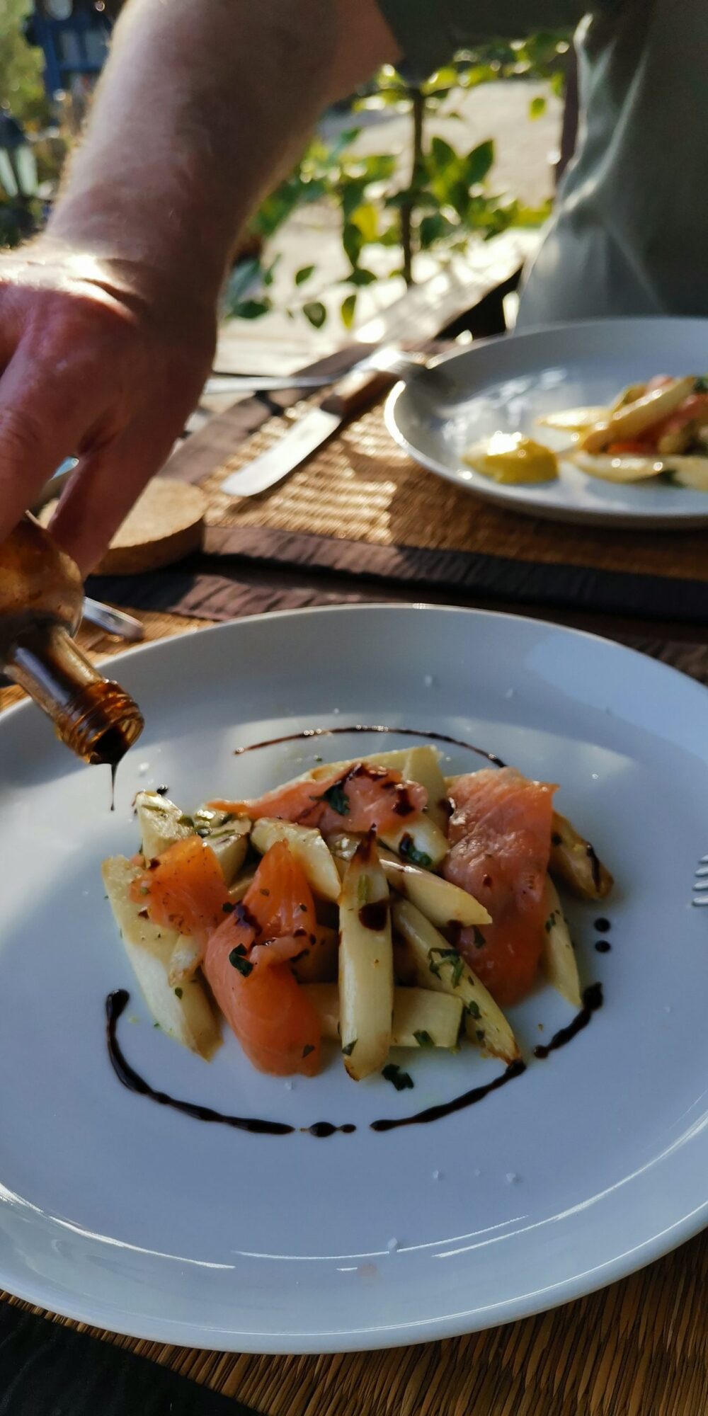 Gebratener Spargel und Räucherlachs. Ein weißer Teller, auf dem der in Scheiben geschnittene schottische Räucherlachs drapiert wurde. Der weiße Spargel liegt dekorativ obenauf. Außen herum wurde ein dünner Faden Balsamico dekoriert.