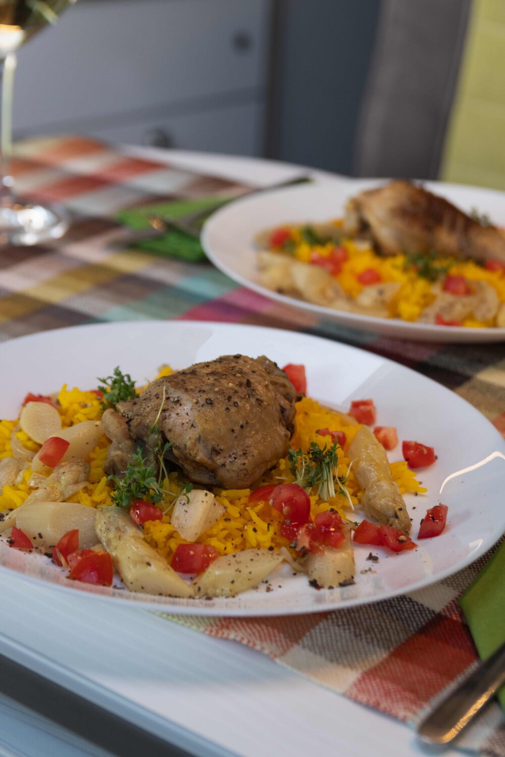 Zitronenhähnchen One-Pot-Gericht. Auf weißem Teller gelber Reis, Tomatenwürfelchen, Spargelstücke, darauf eine Hähnchenkeule.